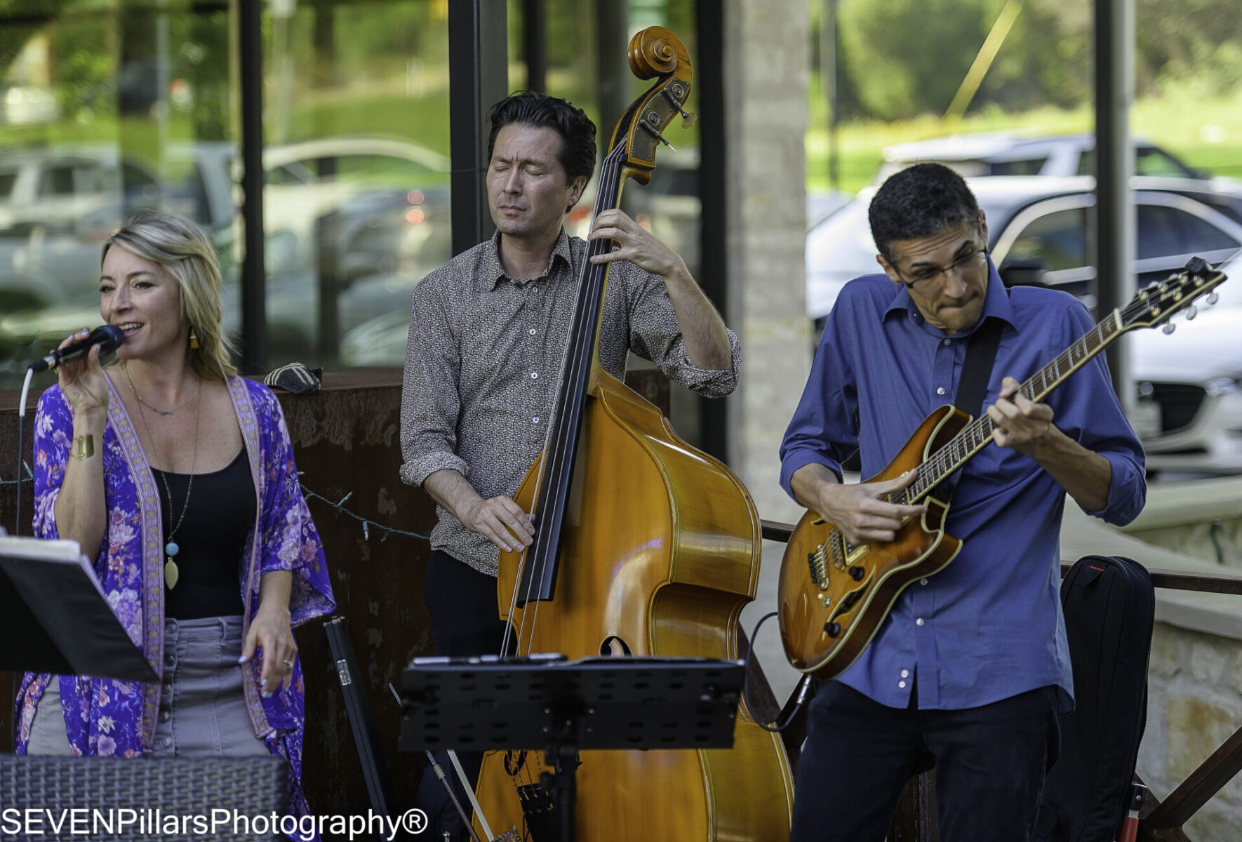 A jazz trio consisting of two men and a lead female vocalist jamming in an outdoor corner street