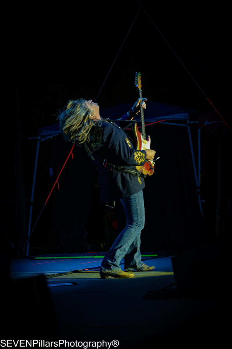 Man with medium-length blond hair bending backwards while jamming on his electric guitar
