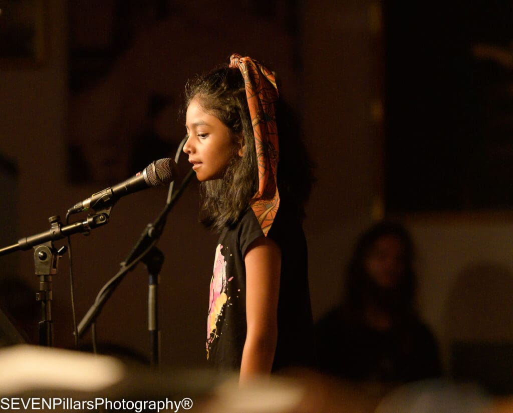 a young girl singing in front of a microphone stand