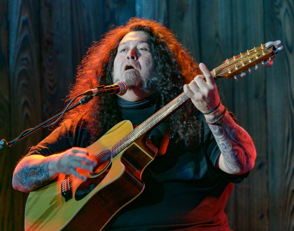 A man with long hair playing an acoustic guitar.