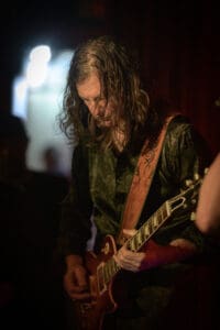 A man with long hair playing an electric guitar.