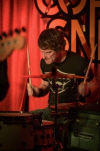 A man playing drums in front of a red curtain.