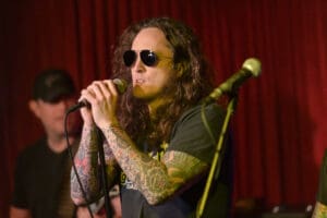 A man with tattoos singing into a microphone.